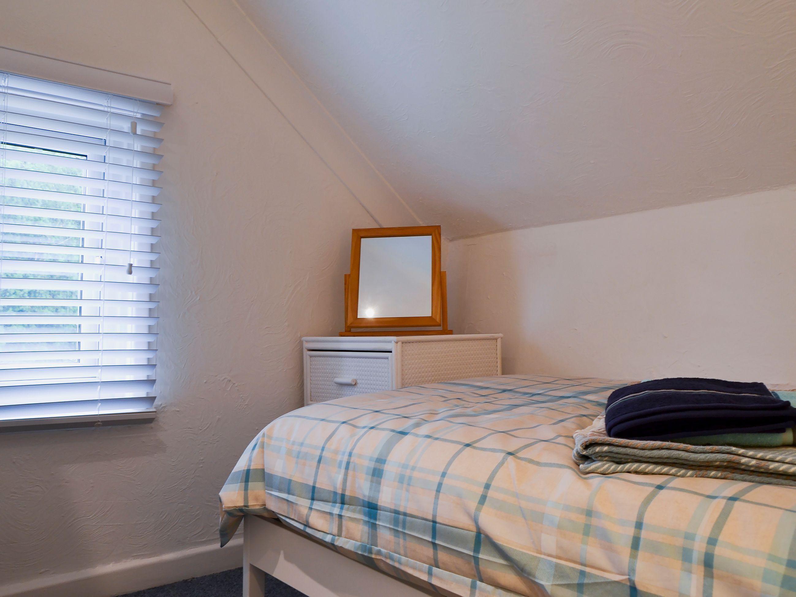 Ein Schlafzimmer mit einem Bett, einem Nachttisch, Jalousien an einem Fenster und einem Spiegel an der Wand.
