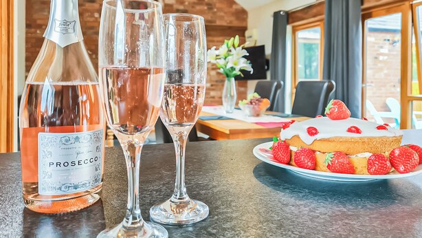 A bottle of prosecco, two glasses, and a strawberry-topped cake on a table. - 1 bedroom accommodation in Charfield, near Wotton-under-Edge (Charfield, near Wotton-under-Edge)