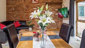 A dining area with a brick wall, a television, and a table set for two with a vase of flowers. - 1 bedroom accommodation in Charfield, near Wotton-under-Edge (Charfield, near Wotton-under-Edge)