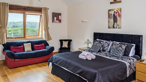A bedroom with a large bed, a sofa, a chair, and a window with curtains. - 1 bedroom accommodation in Charfield, near Wotton-under-Edge (Charfield, near Wotton-under-Edge)