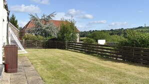 A grassy yard with a wooden fence, a house with a red roof, and a clear blue sky. - 2 bedroom accommodation in Thorncombe, near Broadwindsor (Thorncombe, near Broadwindsor)