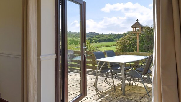 A view from an open door to an outdoor patio with a table and chairs, a clear sky, and a distant view of a landscape with a gazebo. - 2 bedroom accommodation in Thorncombe, near Broadwindsor (Thorncombe, near Broadwindsor)