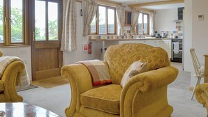 Un sillón amarillo con una manta, una mesa de comedor de madera y vista a una cocina y zona de comedor.