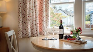 Een ronde tafel met een fles wijn, twee wijnglazen, een fruitschaal en een bloevas.