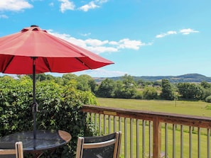A deck with a red umbrella, a table, and chairs, overlooking a grassy field and hills. - 2 bedroom accommodation in Whitwell Farm, Colyford, near Seaton (Whitwell Farm, Colyford, near Seaton)