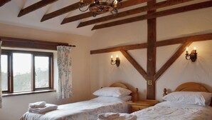 Une chambre avec deux lits, des poutres apparentes, une fenêtre ornée de rideaux à motifs floraux et des lampes fixées au mur.