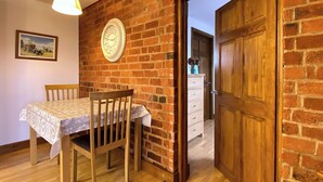 Un coin repas avec une table et des chaises en bois, une horloge au mur et une porte donnant sur une autre pièce.