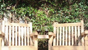 Deux chaises en bois, une table entre les deux, et sur chaque table, un verre de vin rouge.
