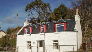 Un bâtiment blanc avec des encadrements de fenêtres rouges et un toit gris, situé près d’une étendue d’eau.