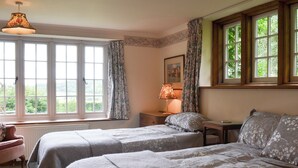 Un dormitorio con dos camas, una ventana con cortinas, una lámpara y un cuadro en la pared.