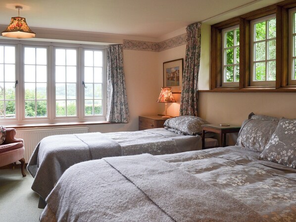 A bedroom with two beds, a window with curtains, a lamp, and a painting on the wall. - 1 bedroom accommodation in Dalwood, near Axminster (Dalwood, near Axminster)