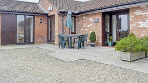 A brick house with a tiled roof, a patio with a table and chairs, and a sign reading 'Brumley Cottage'.