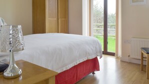 A bedroom with a bed, a wardrobe, a table with a lamp, and a window with a view of greenery.