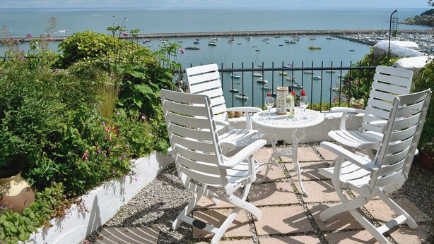 A terrace with white chairs and a table, overlooking a marina with boats. - 2 bedroom accommodation in Brixham (Brixham)