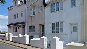 A row of two-story houses with white exteriors, a gated driveway, and a clear sky. - 2 bedroom accommodation in Brixham (Brixham)