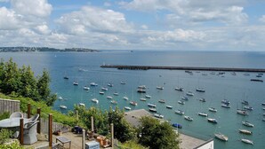 A coastal view with numerous boats docked at a pier, a lighthouse, and a wooden deck with outdoor furniture. - 2 bedroom accommodation in Brixham (Brixham)