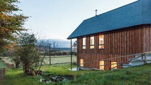 Una casa in legno con tetto spiovente, un camino ben visibile e una scala che conduce all'ingresso.