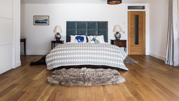 Una camera da letto con un letto grande, due comodini, una testiera, un tappeto, una porta e una lampada a parete.