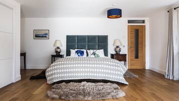 A bedroom with a large bed, two bedside tables, a headboard, a rug, a door, and a wall-mounted lamp.