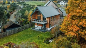 Une cabane en bois dotée d’un balcon, entourée d’un jardin luxuriant et de feuillages d’automne.
