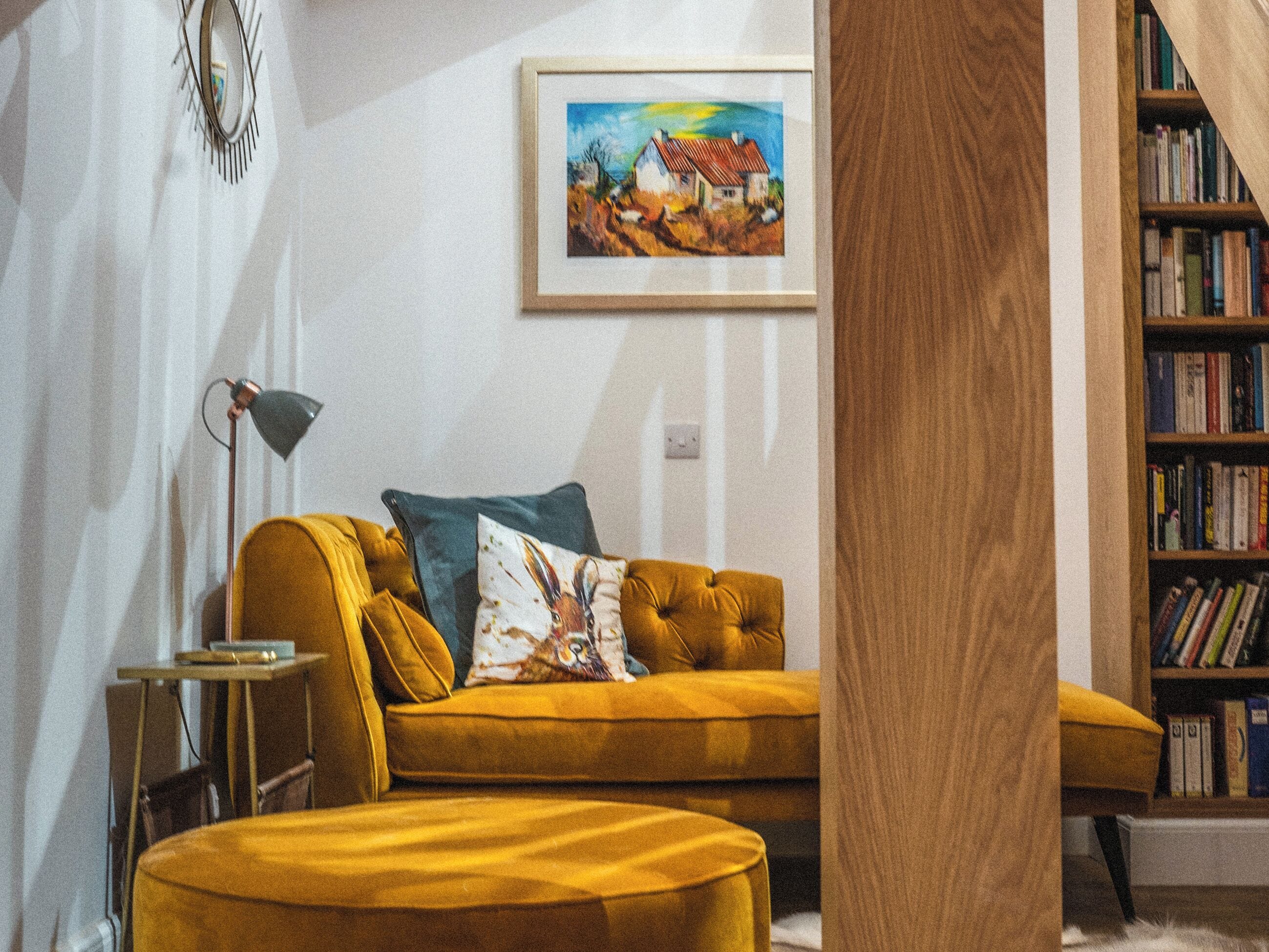 Una sala de estar con un sofá, una lámpara, un cuadro y una estantería.