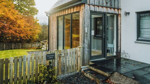 Un chalet avec une façade en bois, une porte d’entrée en verre et un chemin de pierre menant à la porte.