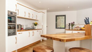 Une cuisine moderne avec des meubles blancs, des poignées en bois, un four encastré et un îlot central en bois avec des tabourets.