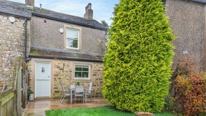 Een stenen huis met een deur, raam en een kleine tuin met een vogelbad.
