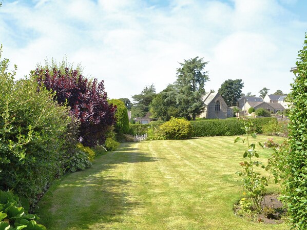 Un jardin bien entretenu, avec une pelouse, divers arbustes et un bâtiment en pierre en arrière-plan.