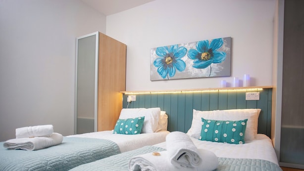 A hotel room with two beds, teal bedding, white pillows with circular patterns, and a wall art of blue flowers. - 2 bedroom accommodation in Shildon, near Bishop Auckland (Shildon, near Bishop Auckland)