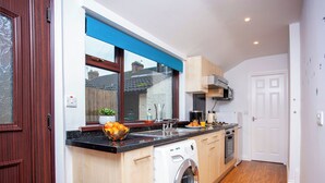 A compact kitchen with a built-in washing machine, a window with blue blinds, and a view of the outside. - 2 bedroom accommodation in Shildon, near Bishop Auckland (Shildon, near Bishop Auckland)