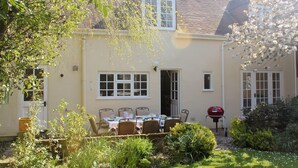 Une maison avec un jardin, une table à manger dressée pour six personnes et un barbecue.