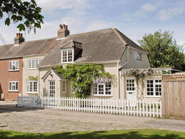 A two-story house with a white picket fence, a brick chimney, and a garden with hanging plants. - 4 bedroom accommodation in Lymington (Lymington)