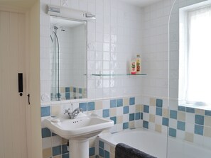 A bathroom with a white sink, a mirror, a shower, and a bathtub. There is a glass shelf with toiletries on it. - 4 bedroom accommodation in Lymington (Lymington)