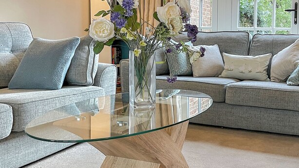 Un salon avec une table basse en verre, des canapés gris et un vase rempli de fleurs.