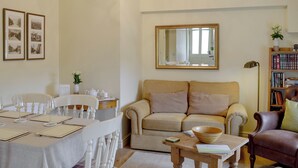 Una sala de estar con una mesa de comedor lista para cuatro personas, un sofá, una mesa de centro y una estantería.