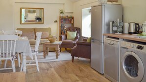 Una sala de estar acogedora con comedor, un sofá, una silla, una estantería, un refrigerador y una lavadora.