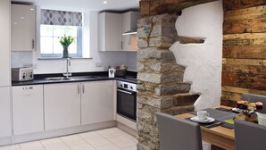 Una cocina moderna con armarios blancos, una pared de piedra, una ventana con una planta y un comedor con mesa y sillas.