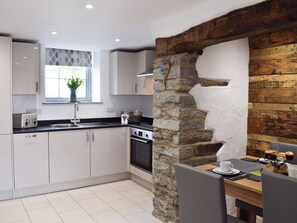 A modern kitchen with white cabinets, a stone wall, a window with a plant, and a dining area with a table and chairs.