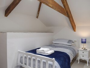A bedroom with a white bed, a blue blanket, a bedside table with a lamp, and exposed wooden beams.