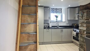 Una cocina con gabinetes grises, una escalera de madera, una pared de piedra y una ventana con un florero.