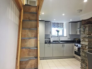 A kitchen with grey cabinets, a wooden staircase, a stone wall, and a window with a flower vase.