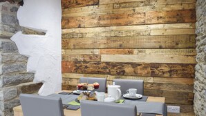 Een eetgedeelte met een rustieke houten wand, stenen details en een tafel voor twee, compleet met waterkoker, kopjes en gebak.