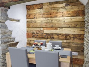 A dining area with a rustic wooden wall, stone accents, and a table set for two with a kettle, cups, and pastries. - 2 bedroom accommodation in Boncath, near Cardigan (Boncath, near Cardigan)
