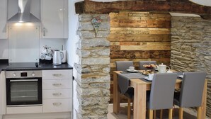 Een keuken met een ingebouwde oven, een eethoek met een tafel en stoelen, en een stenen muur.