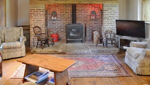 A cozy living room with a brick fireplace, wooden furniture, and a flat-screen TV. - 4 bedroom accommodation in Low Dinsdale (Low Dinsdale)