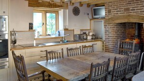 A rustic kitchen with wooden beams, a brick fireplace, and a dining table with chairs. - 4 bedroom accommodation in Low Dinsdale (Low Dinsdale)