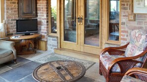 A cozy living area with a brick wall, a television on a wooden table, wicker furniture, and a glass door leading outside. - 4 bedroom accommodation in Low Dinsdale (Low Dinsdale)