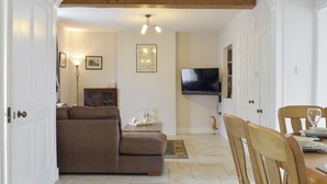 A living room with a sofa, a television mounted on the wall, and a dining area with a table and chairs. - 3 bedroom accommodation in Bampton, near Witney (Bampton, near Witney)