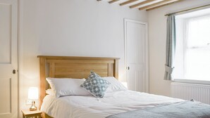 A bedroom with a wooden bed frame, white bedding, a bedside lamp, and a window with curtains. - 3 bedroom accommodation in Bampton, near Witney (Bampton, near Witney)